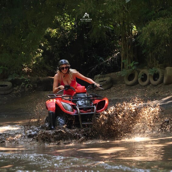 A person riding an ATV through a shallow water body, surrounded by dense greenery. 5