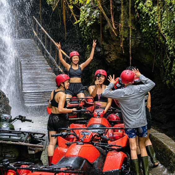 A group of people in red helmets and life jackets on a red ATV, standing on a stone staircase with a waterfall in the background. 2