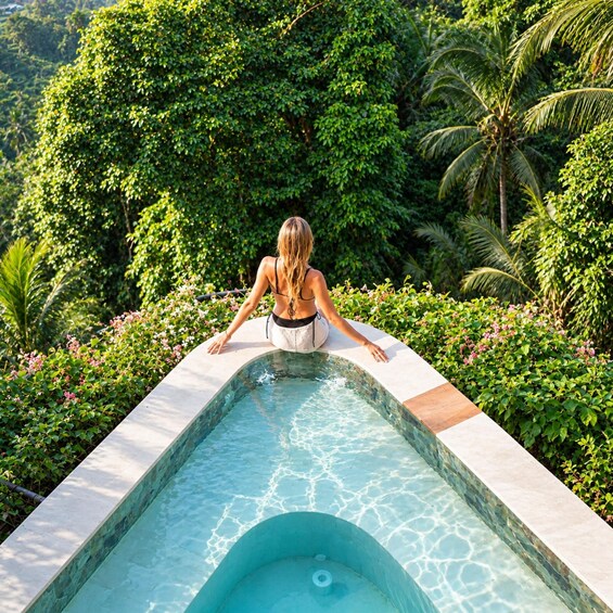 A woman in a bikini at the edge of a swimming pool surrounded by lush greenery. 5
