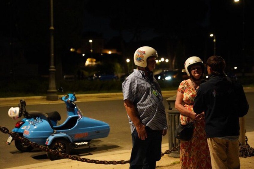 A blue scooter chained to a pole, a person in a patterned shirt, and two individuals in a conversation. 2