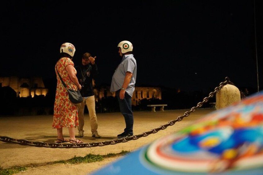 Three people standing on a sandy area with a chain barrier in the foreground. 3