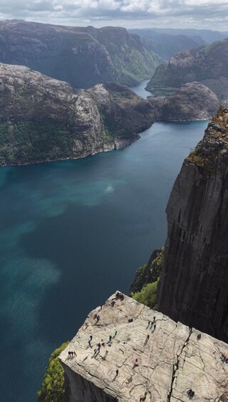 A group of climbers on a cliff overlooking a deep blue fjord surrounded by rugged mountains. 3