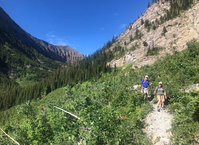 Two hikers on a rocky trail surrounded by dense forest and mountains. 5