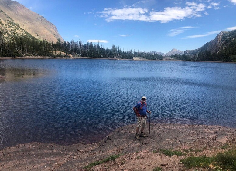 A man standing by a calm lake with mountains in the background. 3