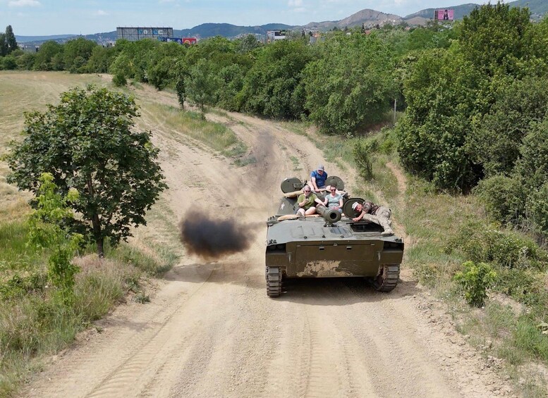 A military vehicle on a dirt road with smoke, surrounded by greenery and hills. 4
