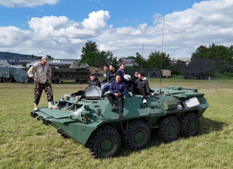 A group of people on a military vehicle with a grassy field and a cloudy sky in the background. 5