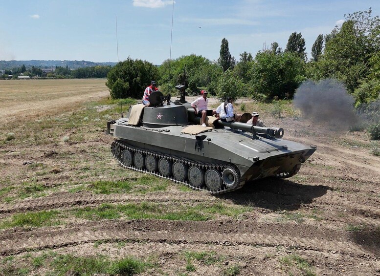 A military tank on a dirt road with people sitting on it. 1