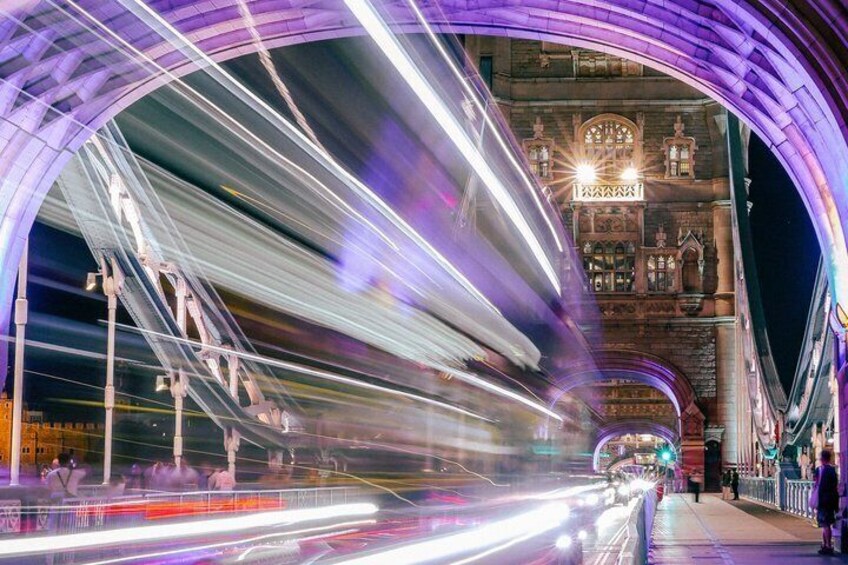 Un pont illuminé par les traînées de lumière des véhicules en mouvement, un bâtiment historique doté d’arches et de fenêtres en plein cintre, et une passerelle piétonne. 4
