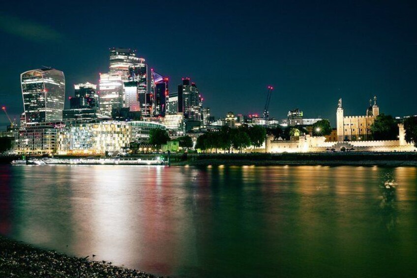 Une vue nocturne sur les gratte-ciel d’une ville, avec les bâtiments illuminés qui se reflètent dans l’eau. 3
