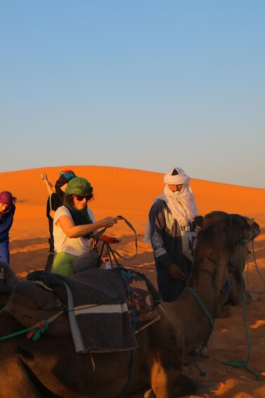 A camel caravan in a desert with people riding camels. 1