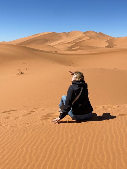 A person sitting on a sand dune in a desert landscape. 4
