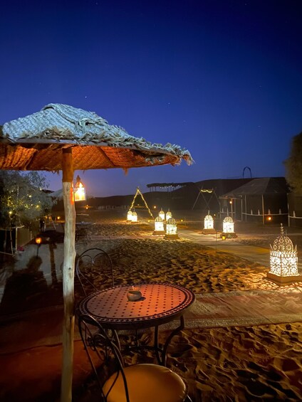 A beachside dining area with a thatched umbrella and metal table and chairs. 2