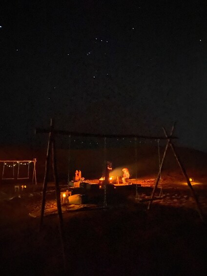 A nighttime scene with a swing set, a campfire, and a distant building. 5