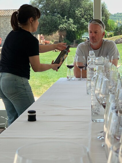 A woman pouring wine into a glass at an outdoor table with multiple glasses and bottles. 5