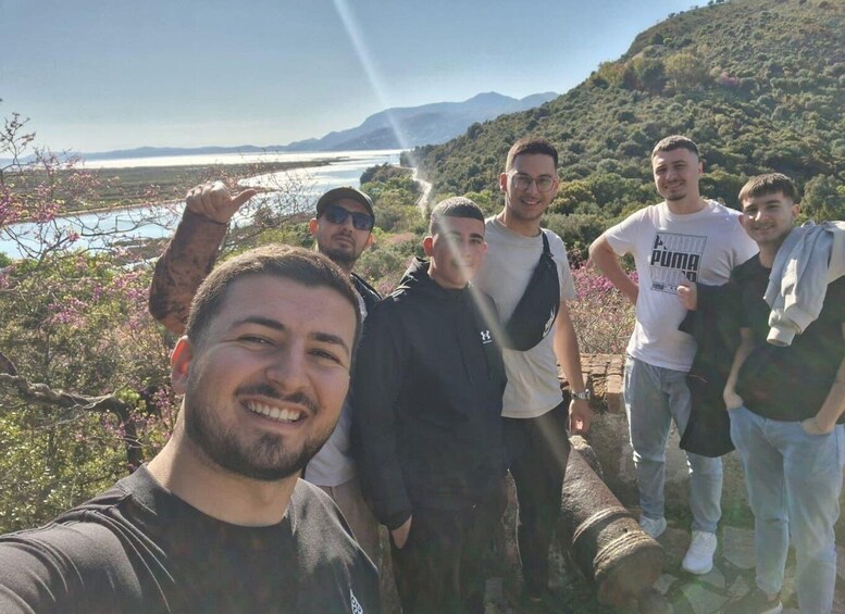 A group of people standing on a rocky outcrop overlooking a body of water and hills. 1