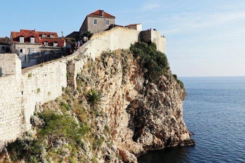 A coastal fortification with a steep cliff, a stone wall, and a building with red-tiled roofs. 4