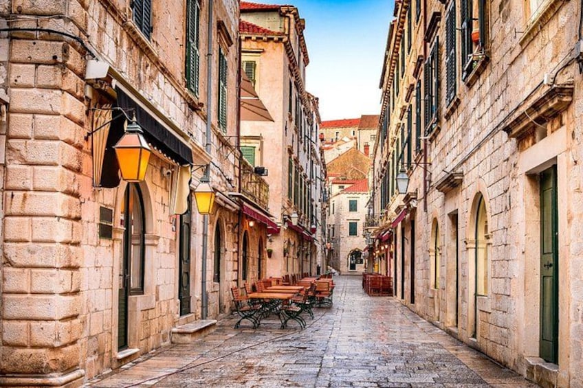 A cobblestone street lined with historic buildings, a wooden bench, and hanging street lamps. 5