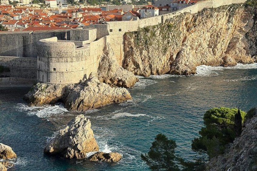A coastal city with a historic stone wall, rocky coastline, and red-roofed buildings. 3