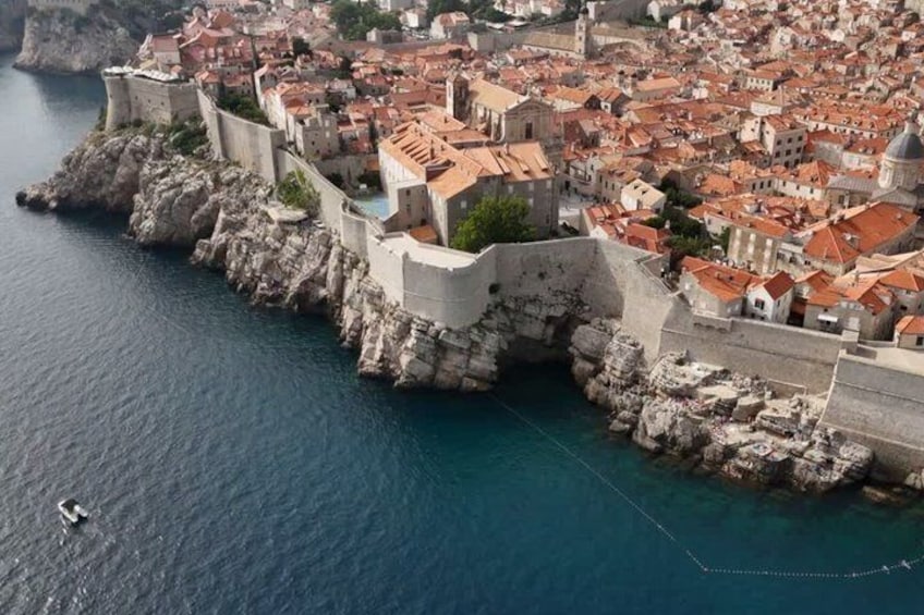 A coastal city with historic buildings, a fortified wall, and a clear blue sea. 1