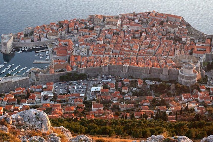 A coastal city with a fortified wall, red-roofed buildings, and a harbor with boats. 2
