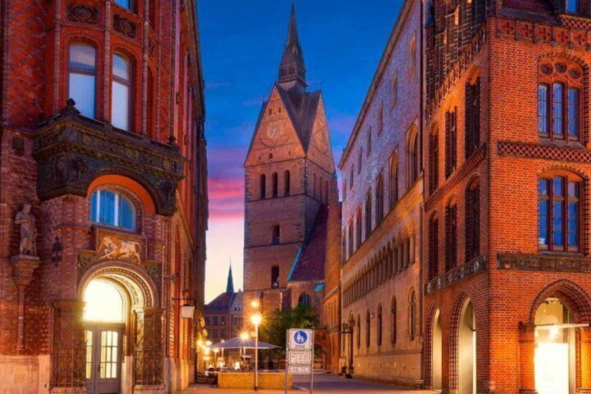 A historic street with brick buildings, a church spire, and a sunset sky. 1