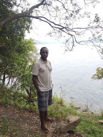 A man standing by a lake with trees and rocks around him. 2
