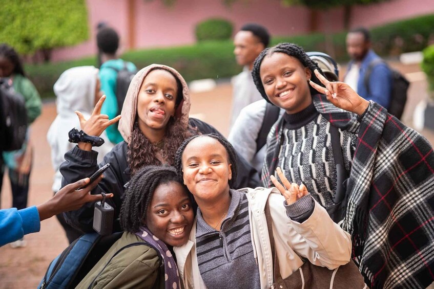 A group of people outdoors, some making peace signs, with greenery and a building in the background. 5