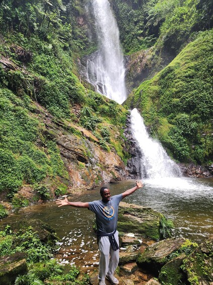 A waterfall in a lush green valley with a person standing with arms outstretched. 4