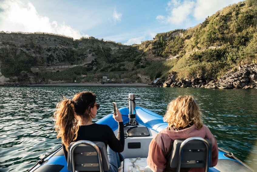 Two people on a blue inflatable boat on a calm river, surrounded by hills with sparse vegetation. 3