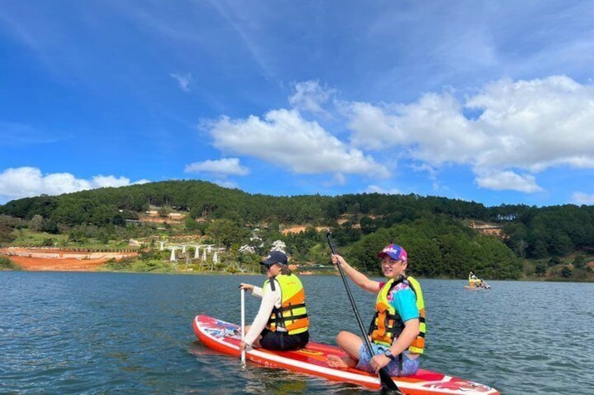 Two people on a paddleboard in a lake with a forested hillside in the background. 1