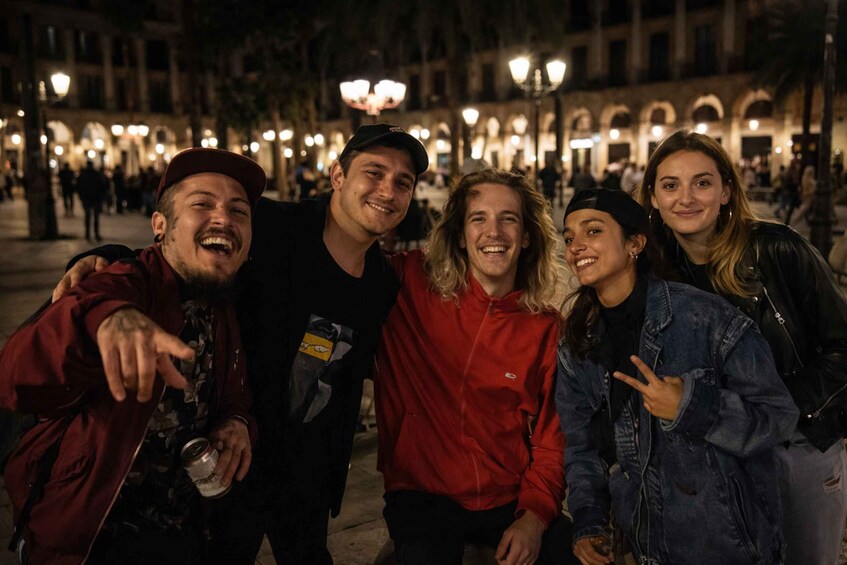 A group of people posing in a public square at night with street lamps and buildings in the background. 1
