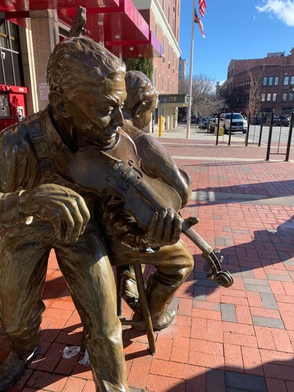 A bronze statue of two figures, one holding a rifle, seated on a brick pavement. 5