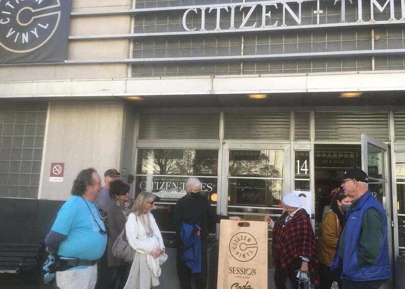 A group of people outside a building with a sign that reads 'CITIZEN+TIM.' 3