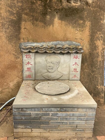 A stone monument with a carved figure and inscriptions, set against a textured wall. 3