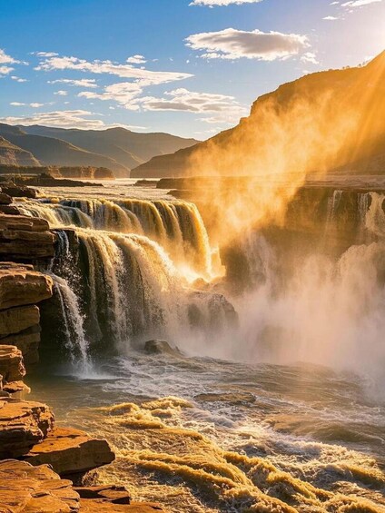 A waterfall cascading over rocky terrain with sunlight illuminating the scene. 1