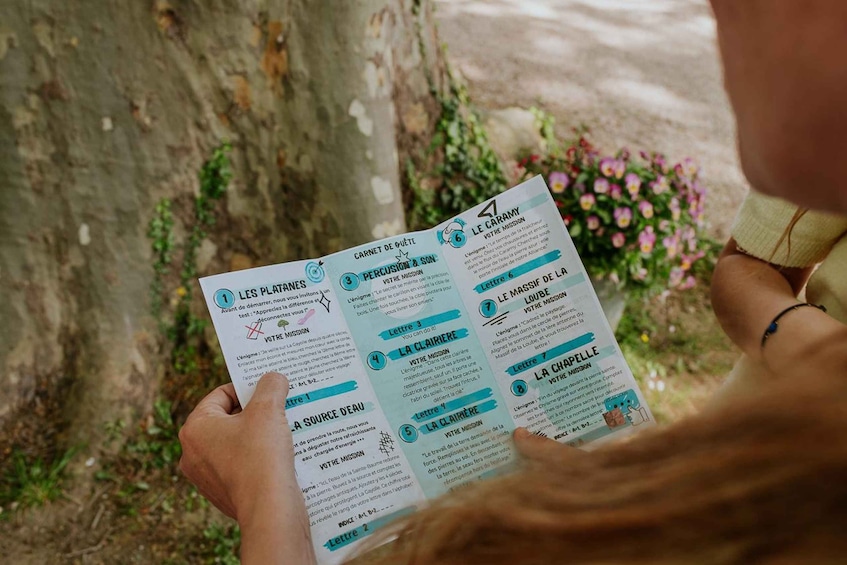 A person holding a pamphlet with text and illustrations, outdoors with a tree and flowers in the background. 4