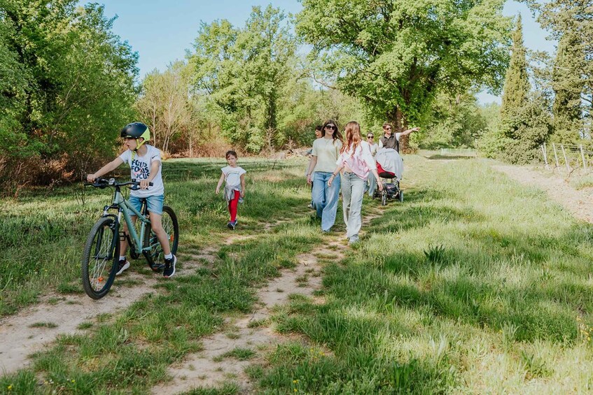A group of people walking and cycling on a dirt path in a grassy area with trees. 2