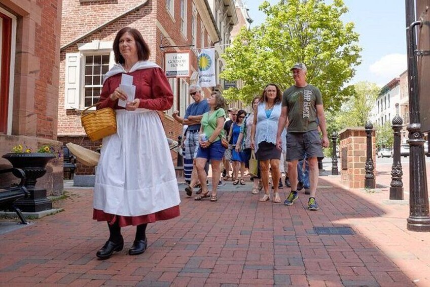 A person in historical costume walking on a brick street with pedestrians in the background. 2
