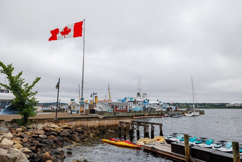 Een Canadese vlag, een steiger met kajaks, een vissersboot en een rotsachtige kustlijn. 1