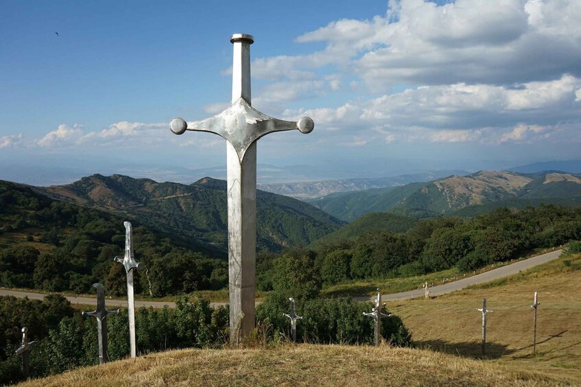 A large cross with a sword on top, surrounded by smaller crosses, set against a mountainous landscape. 4