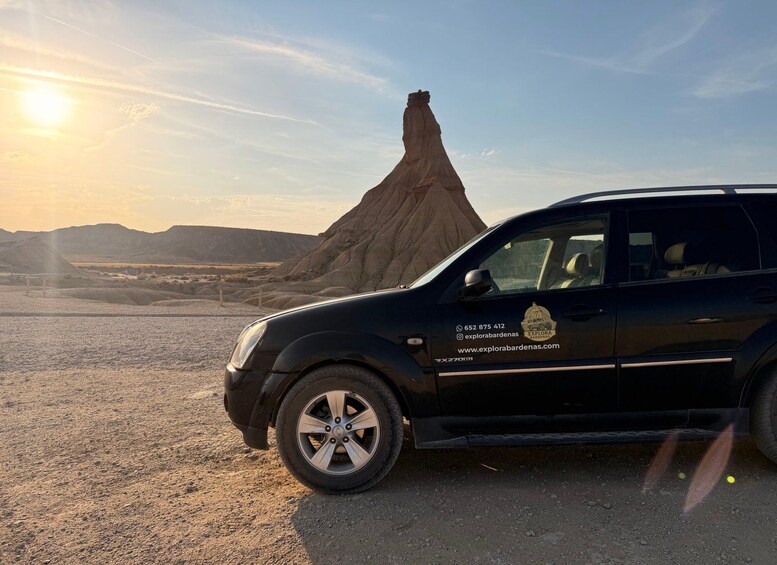 A black SUV parked on a gravel road with a large rock formation in the background. 5