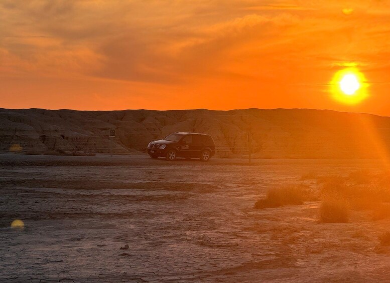 A vehicle on a dirt road during sunset with a mountainous backdrop. 1