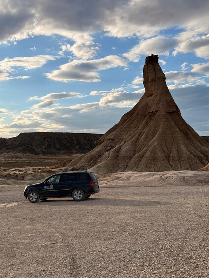 A black SUV parked in a gravel area with a large rock formation in the background. 2
