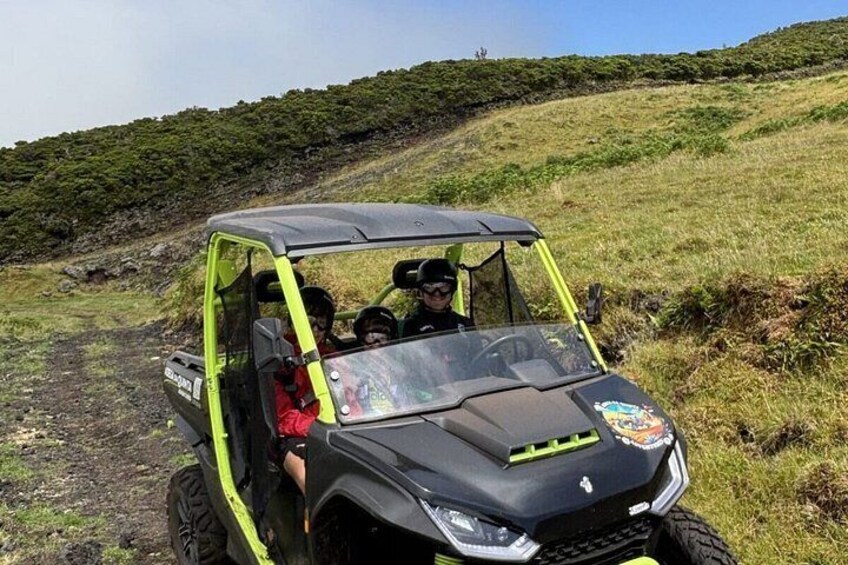 A black and yellow off-road vehicle on a dirt path with a hilly landscape in the background. 1