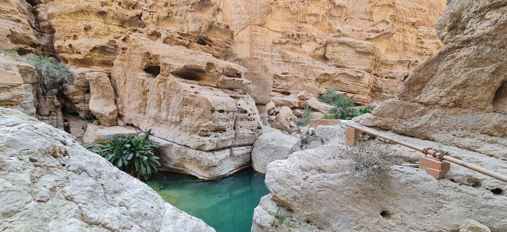 A canyon with a turquoise pool, rocky formations, and a wooden walkway. 2