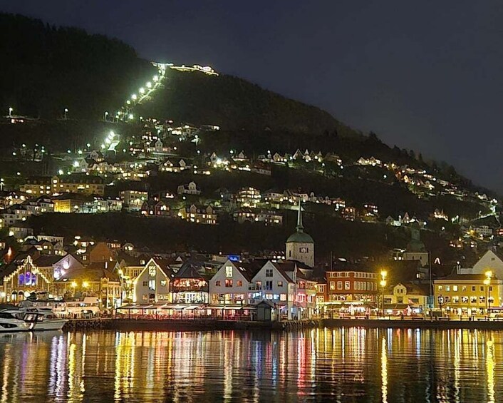 A coastal town at night with illuminated buildings and a hill in the background. 2