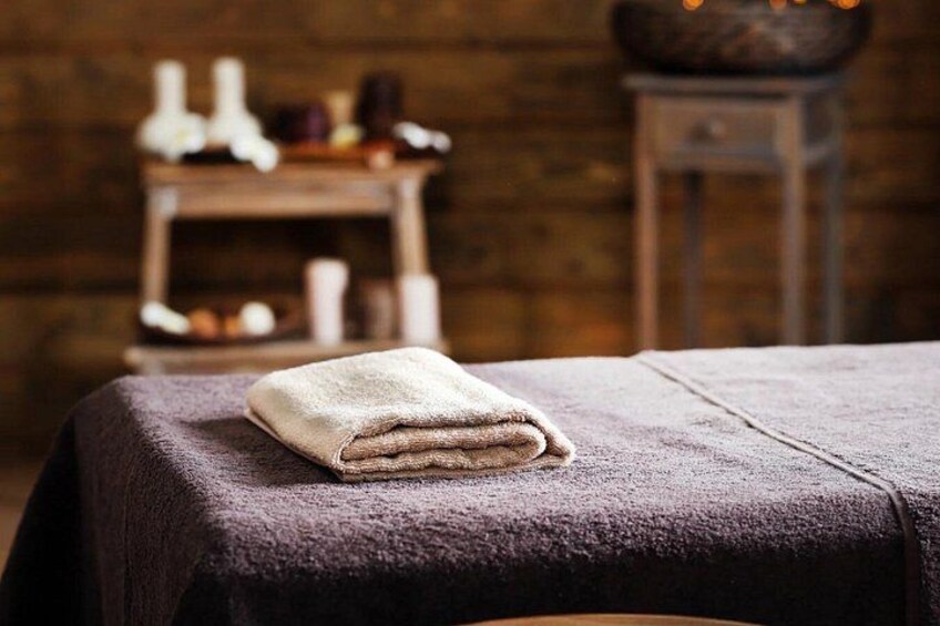 A neatly folded towel on a bed with a dark blanket, a wooden shelf with candles, and a rustic wall in the background. 1
