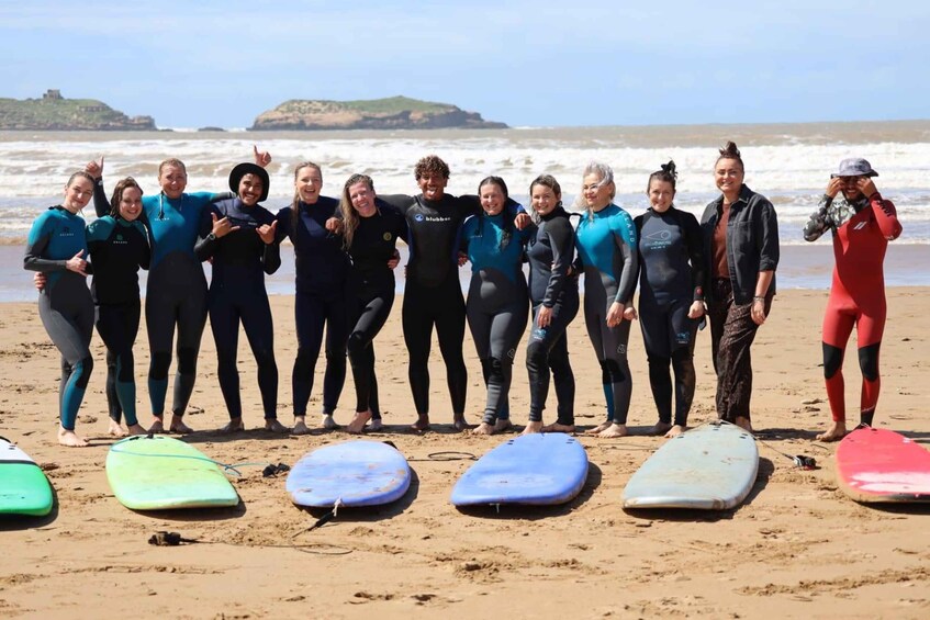 A group of people in wetsuits on a beach with surfboards and ocean waves in the background. 5