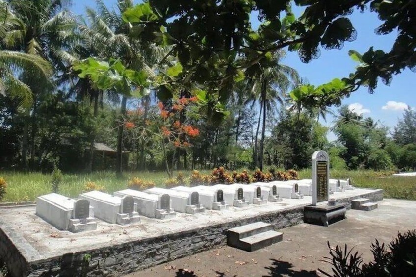 A row of white tombstones with a central monument in a tropical garden setting. 2