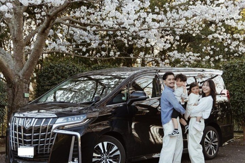 A black minivan with a family of four standing in front of it. 2